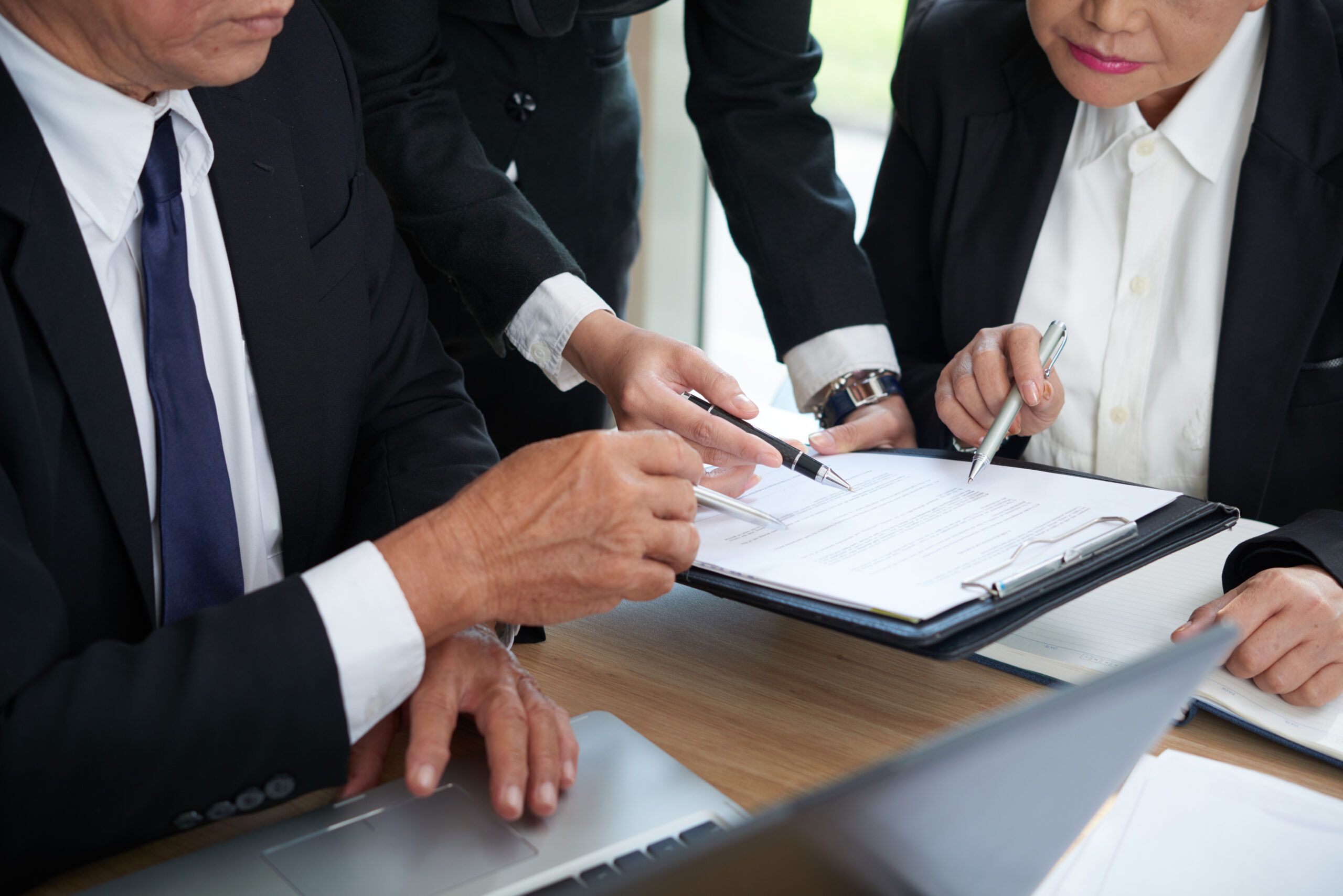 Three people reviewing a business contract document together, symbolizing careful examination to prevent fraudulent practices.