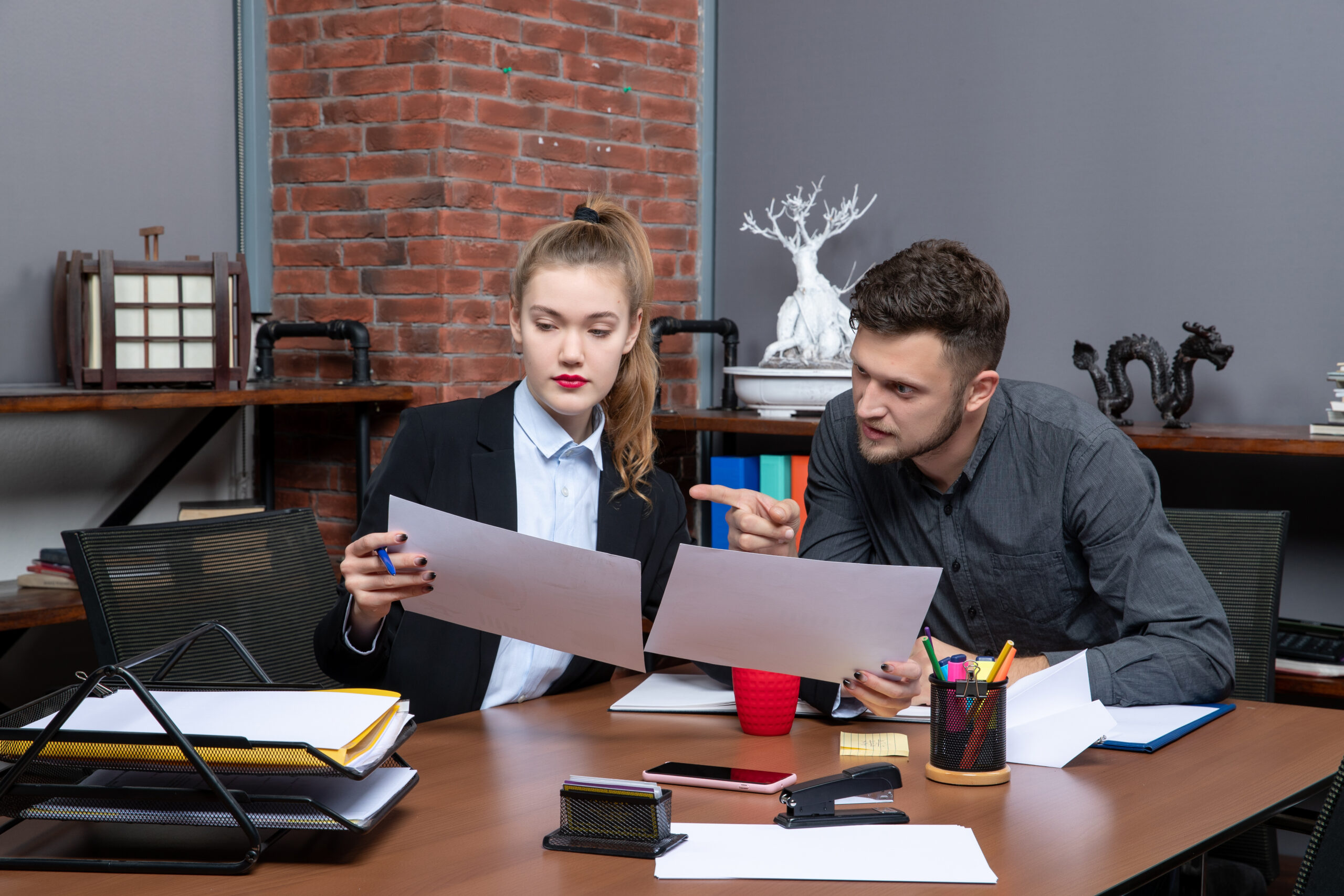 Two office employees reviewing documents and discussing business issue at desk