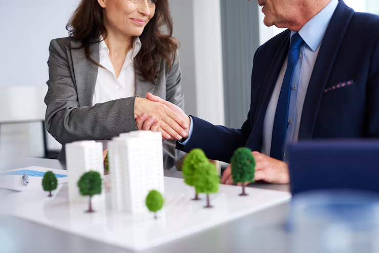 Business partners shaking hands over architectural model during successful real estate development meeting