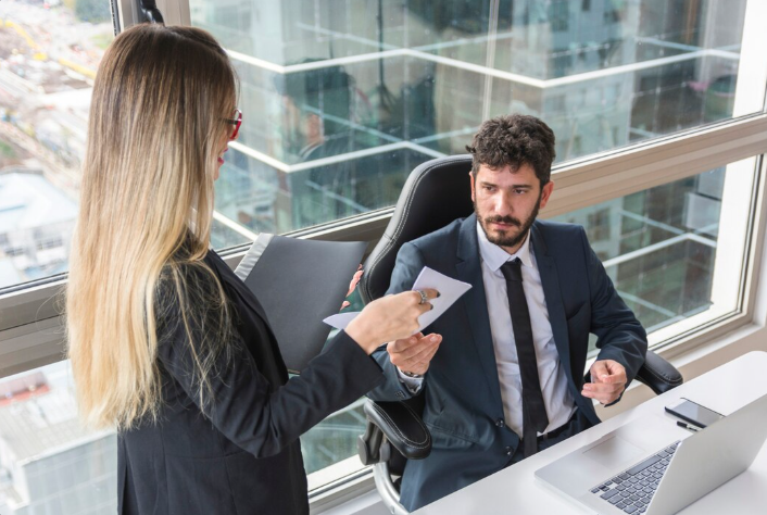 A Business Litigation Attorney NYC in a blue suit receiving legal documents from a female colleague in a high-rise office overlooking the city.