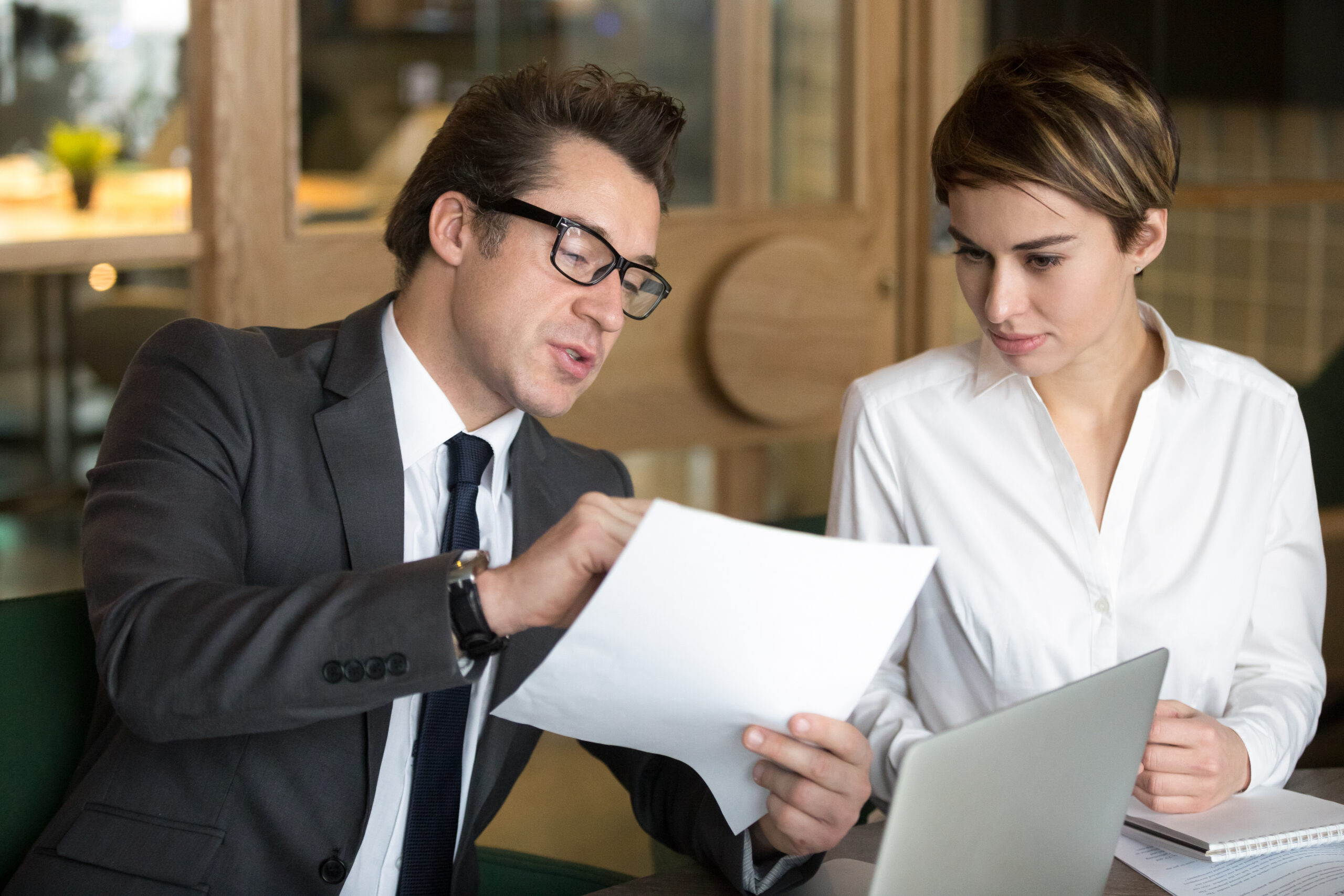 A professional lawyer in a suit and glasses explaining property contract conditions to a female client during a legal consultation.