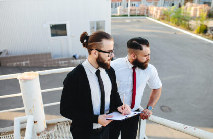 Two businessman at work Two professional men standing on an outdoor platform, one writing on a clipboard while the other looks toward the background.