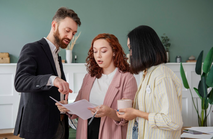 Three legal professionals reviewing a commercial property lease agreement together in a modern office, with a man pointing out specific clauses in the documents.