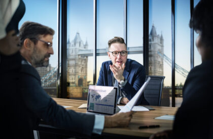 business-meeting-london (2) "Business executives discussing corporate strategy in a modern London office with Tower Bridge view, reviewing company growth reports during a professional boardroom meeting."