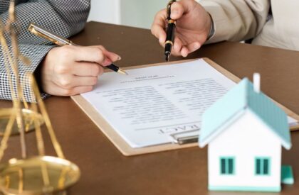 1 Clients signing a real estate purchase agreement during a property closing with legal documents, a house model, and scales of justice on the desk.
