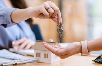 2 Real estate agent handing over house keys to a new homeowner during a property purchase closing with a model home and contract documents.