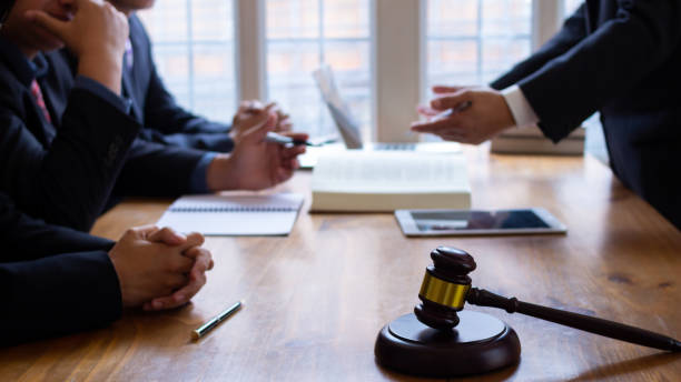 Attorney consulting with clients during a legal meeting with a judge's gavel, documents, and digital devices on the conference table.