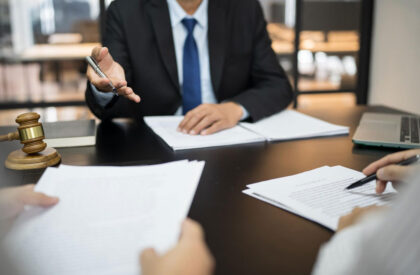 4 A professional consultation scene showing an attorney extending a pen toward a client's contract on a desk, with a judge's gavel and laptop in the background, representing legal services and contract signing.