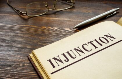 Legal document titled "Injunction" placed on a wooden desk with glasses and a pen
