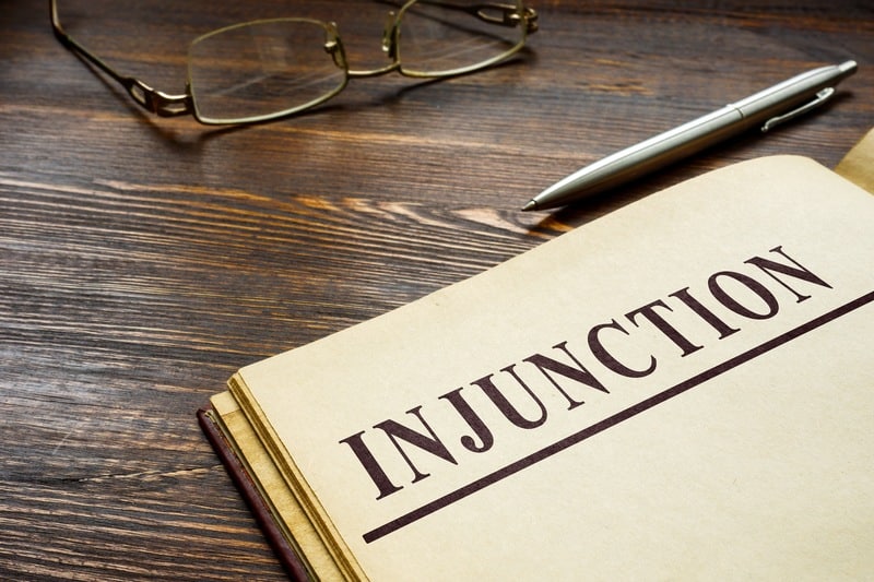 Legal document titled "Injunction" placed on a wooden desk with glasses and a pen